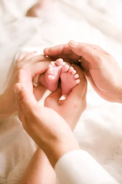 妈妈和爸爸的手正抱着一个刚出生的婴儿在一张白床上的小可爱腿 快乐的母亲 — 图库照片