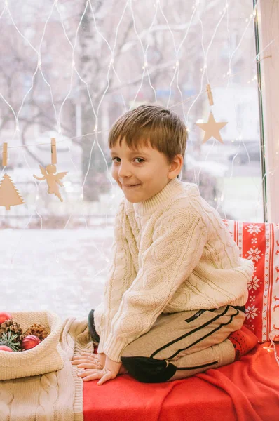 Roztomilý Chlapeček Teplém Bílém Pleteném Svetru Sedí Doma Okna Zdobeného — Stock fotografie