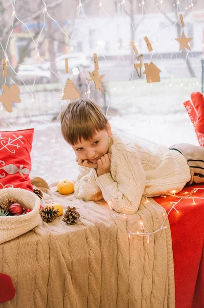 Roztomilý Chlapeček Teplém Bílém Pleteném Svetru Sedí Doma Okna Zdobeného — Stock fotografie