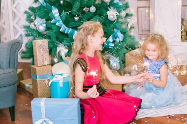 Beyaz balo elbisesi içinde, Noel ağacının yanında, hediye ve gümüş konfetiyle güzel, sarı saçlı kızlar. Noel havası