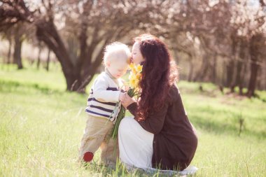 Bahar çiçekleri olan bir aile. Uzun siyah saçlı, küçük bir oğlu olan genç bir anne baharda bebeğine sarılıyor. Bahar havası. Anneler Günü