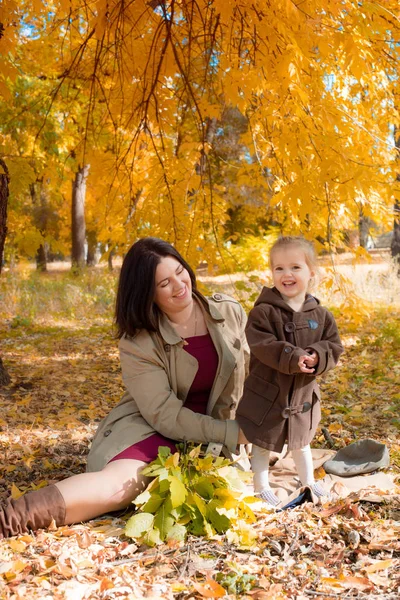 Family in the autumn park among yellow leaves. Young mother with a little daughter play with leaves in the autumn park. Autumn mood