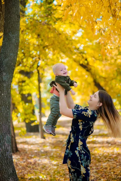 Family in the autumn park among yellow leaves. Young mother with a little son play with leaves in the autumn park. Autumn mood