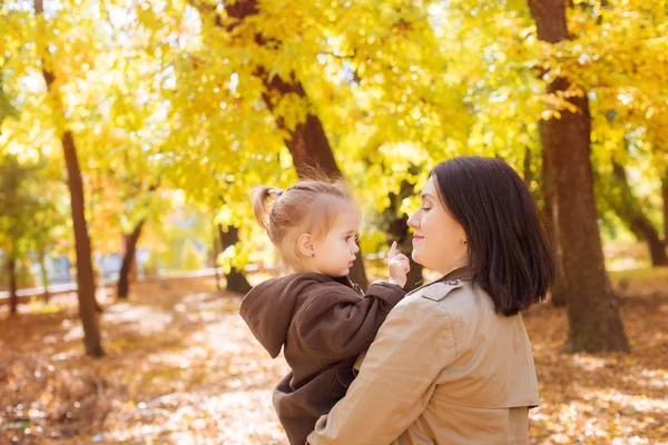 黄色の葉の間の秋の公園で家族 幼い娘を持つ若い母親は秋の公園で葉と遊ぶ 秋の気分 — ストック写真