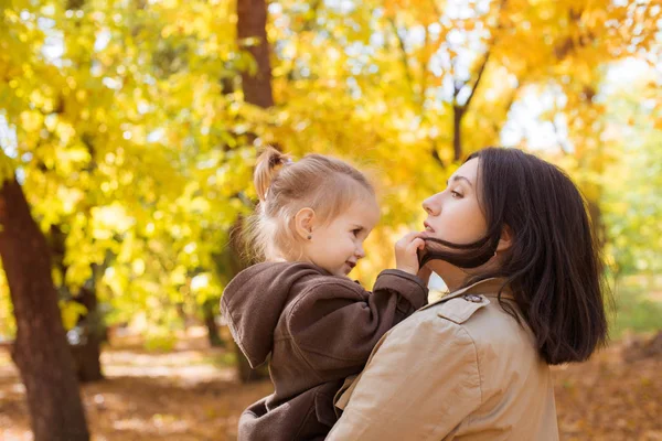 Family in the autumn park among yellow leaves. Young mother with a little daughter play with leaves in the autumn park. Autumn mood