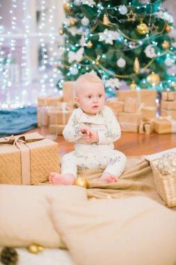 Noel ağacının orada elinde hediyeler ve oyuncaklarla oturan küçük çocuk. Noel havası