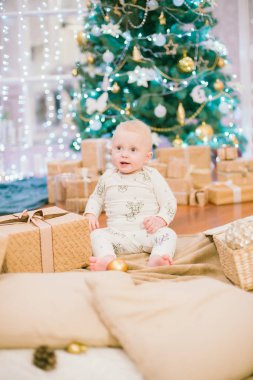 Noel ağacının orada elinde hediyeler ve oyuncaklarla oturan küçük çocuk. Noel havası