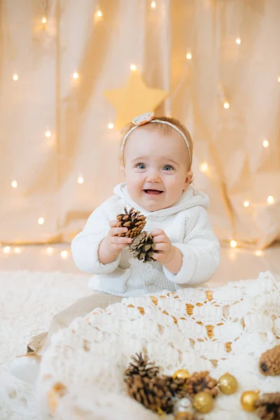 一个一岁的可爱小女孩 头戴鲜花 头戴浅色针织毛衣 头戴绷带 坐在那里玩冷杉球果 节日气氛 圣诞快乐 — 图库照片