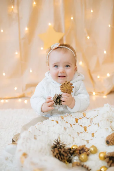 一个一岁的可爱小女孩 头戴鲜花 头戴浅色针织毛衣 头戴绷带 坐在那里玩冷杉球果 节日气氛 圣诞快乐 — 图库照片