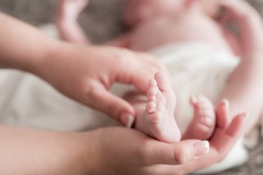 Annelik elleri evde bebek bacaklarını yatakta tutuyor. Mutlu ve sağlıklı annelik. Çocuk bakımı