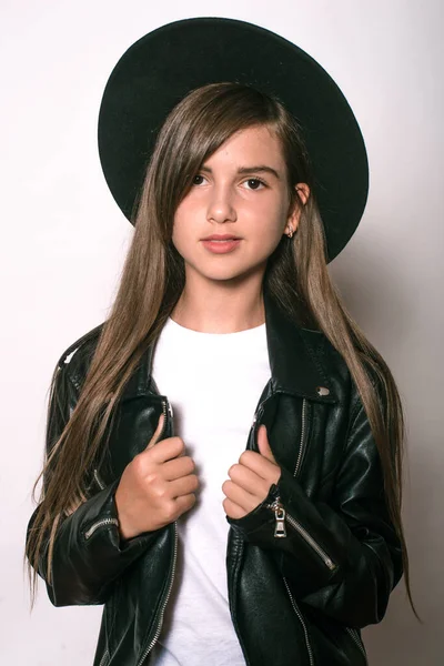 A teenage girl in a trendy leather jacket and an even hat on a white background. Teenage fashion. Street fashion. Beauty and fashion