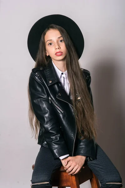 A teenage girl in a trendy leather jacket and an even hat on a white background. Teenage fashion. Street fashion. Beauty and fashion