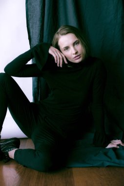 Sarı saçlı, çıplak makyajlı, siyah dizli, siyah pantolonlu, beyaz ve siyah arka planda stüdyoda poz veren çekici bir manken.