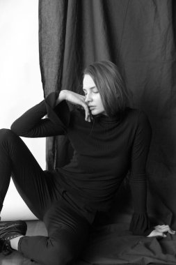 Sarı saçlı, çıplak makyajlı, siyah dizli, siyah pantolonlu, beyaz ve siyah arka planda stüdyoda poz veren çekici bir manken.