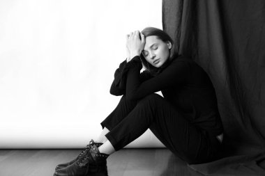 Sarı saçlı, çıplak makyajlı, siyah dizli, siyah pantolonlu, beyaz ve siyah arka planda stüdyoda poz veren çekici bir manken.