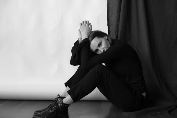 Young attractive girl model with blond hair and nude makeup in black knee-highs black trousers posing in the studio on a white and black background