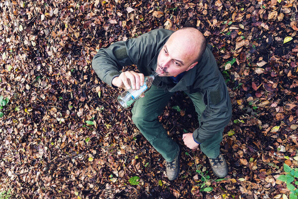 Drunk man sits and drinks from a bottle