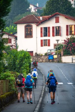 Pilgrims with backpack walking the Camino de Santiago, Saint Jean Pied de Port in Pays Basque, France clipart