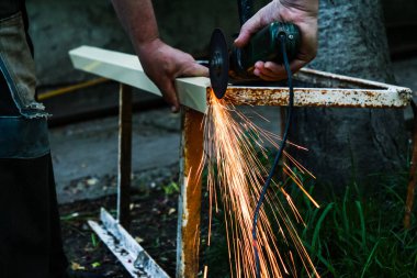 Bir adam dairesel testereyle metal bir köşeyi keser, kıvılcımlar uçuşur.