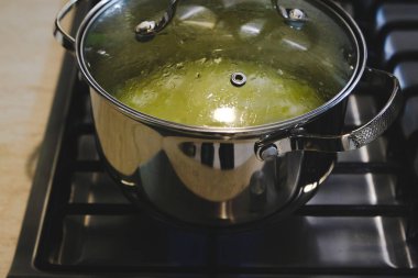 Metal bir tava ocağın üzerinde duruyor, altında mavi bir alev yanıyor.