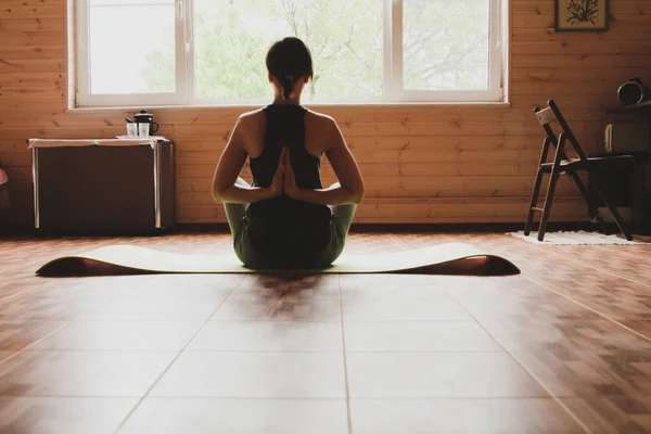 Genç bir kadın, bahçeye bakan büyük bir pencerenin önünde sabah egzersizlerine, yogaya, forma girmeye hazırlanıyor.