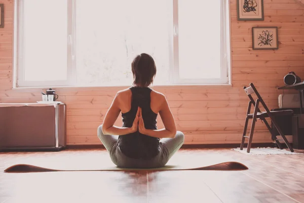 A young woman is engaged in morning exercises - exercises, yoga, fitness - at home in front of a huge window overlooking the garden