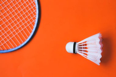 Turuncu arka planda beyaz badminton topu ve raket. Kavram: minimalizm, yaz açık hava oyunları