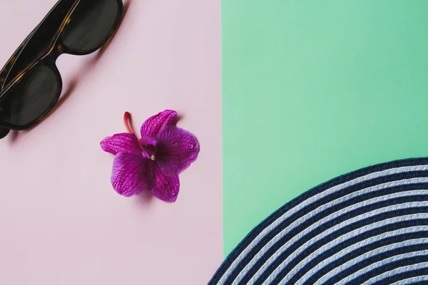 Summer flat lay: orchid flower, sunglasses and a sun hat on a pink-green background. Concept: summer vacation at sea in the tropics