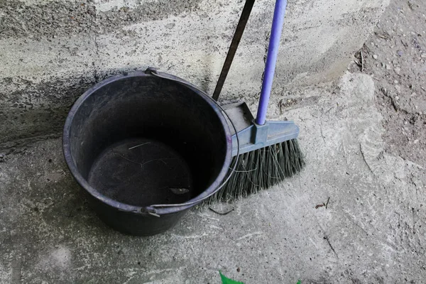 Boş plastik çöp kutusu süpürge ve faraş yanında duruyor.