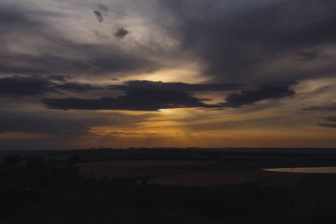 Batan güneşin ışınları tarlaların üzerindeki bulutları delip geçiyor.