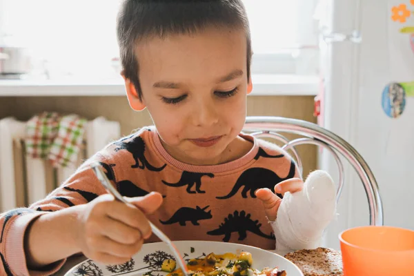 Bir çocuk mutfakta masada oturur ve çırpılmış yumurta ve sebzelerle kahvaltı eder.
