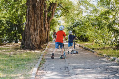 İki küçük şapkalı çocuk şehir caddesinde scooter kullanıyor.