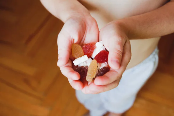 Çocuk elinde beyaz çiğnenebilir vitaminler ve çok renkli jelatinli vitaminler tutuyor.