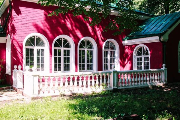 Cozy white and red house with arched semicircular windows, white balconies railing, immersed among the trees