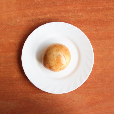 Kahverengi ahşap bir masada duran beyaz bir tabakta etli yuvarlak bir turta yatıyor.