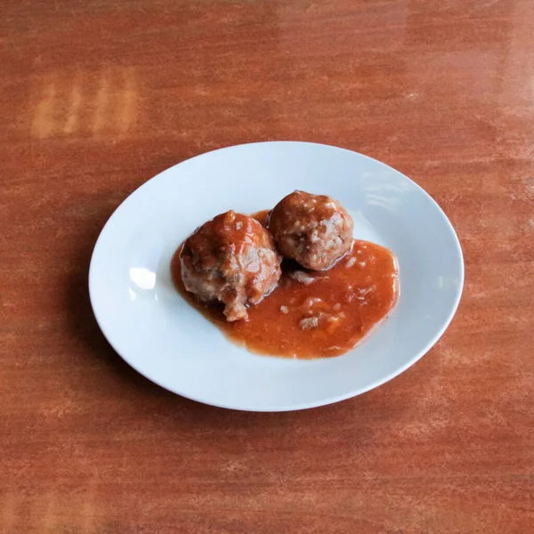 Beyaz tabakta domates sosunda köfteler var.