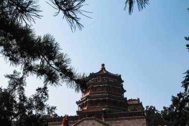Yiheyuan Parkı 'ndaki Çin imparatorlarının evinin tepesindeki yeşil ağaçlar tarafından çerçevelenmiş bir pagoda.
