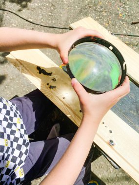 Bir çocuk sokakta oturur ve bir tahta parçasını yakmak için büyüteç kullanır.