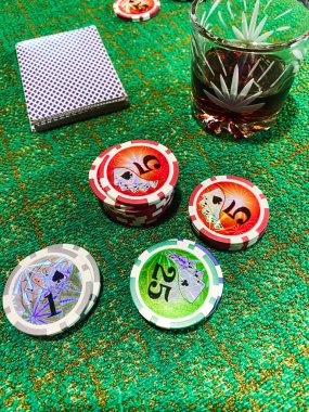 Yeşil kumaşın üzerinde bir deste kağıt ve cips var, yanında da bir bardak alkol.