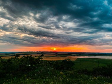 Koyu mavi kasvetli bulutlarda batan güneşin turuncu diski.