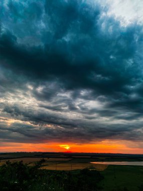Koyu mavi kasvetli bulutlarda batan güneşin turuncu diski.