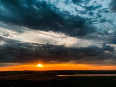 Koyu mavi kasvetli bulutlarda batan güneşin turuncu diski.