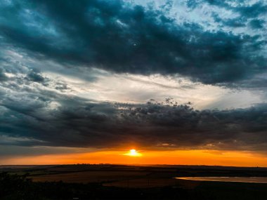 Koyu mavi kasvetli bulutlarda batan güneşin turuncu diski.