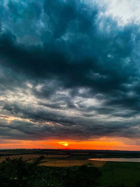 Koyu mavi kasvetli bulutlarda batan güneşin turuncu diski.