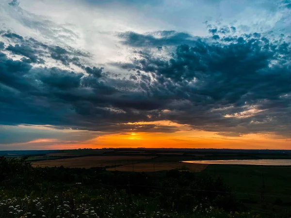 Koyu mavi kasvetli bulutlarda batan güneşin turuncu diski.
