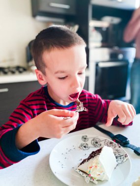 Çocuk pijamalarıyla mutfakta oturuyor ve bir parça pasta yiyor.