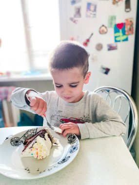 Çocuk pijamalarıyla mutfakta oturuyor ve bir parça pasta yiyor.