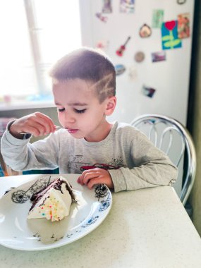 Çocuk pijamalarıyla mutfakta oturuyor ve bir parça pasta yiyor.