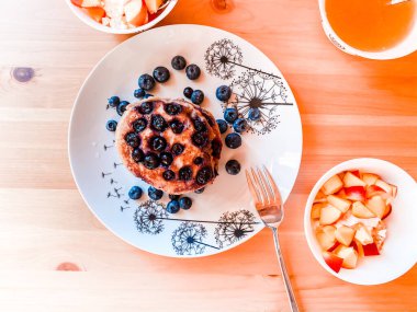 Tahta bir masada, krep, yaban mersini, meyve kasesi ve bir çaydanlık yeşil çay.