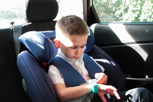 Küçük çocuk çocuk çocuk koltuğunda arabada oturur ve kol saatine bakar.